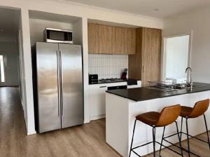 a kitchen with a stainless steel refrigerator and two bar stools at Wonderful Jubilee Estate House in Wyndham Vale