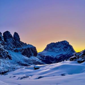 a snow covered mountain range with a house in the foreground w obiekcie Rifugio Frara w mieście Selva di Val Gardena