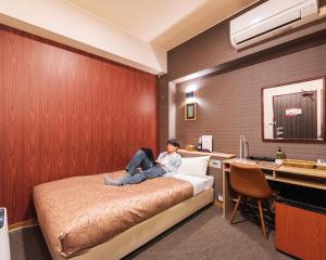 a woman sitting on a bed in a hotel room at HOTEL RELIEF Kokura Station in Kitakyushu