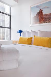 a white bedroom with a large bed with yellow pillows at Placemakr Wall Street in New York