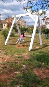 Une petite fille assise sur une balançoire dans une cour dans l'établissement Apartments Kruno, à Međugorje