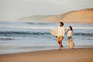 un hombre y una mujer caminando por la playa con una tabla de surf en RACV Torquay Resort, en Torquay