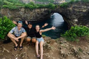 três pessoas sentadas num penhasco em frente a uma caverna em citiz house & hostel em Nusa Penida