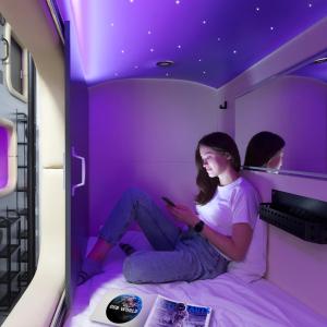 uma mulher sentada numa cama num quarto roxo em Capsule Hotel Constellation 89 em Lviv