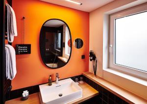 La salle de bains orange est pourvue d'un lavabo et d'un miroir. dans l'établissement Hotel Zugbrücke Grenzau GmbH, à Höhr-Grenzhausen