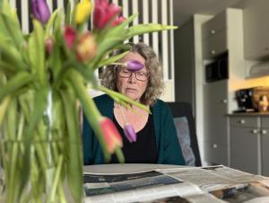 une femme âgée assise à une table avec un vase de fleurs dans l'établissement Fijne Studio aan zee, à Callantsoog