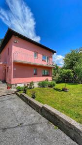 une maison rose avec une cour d'herbe devant elle dans l'établissement Guest House Bosnian House, à Sarajevo