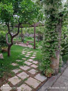 un chemin en pierre dans un jardin avec des arbres et une pergola dans l'établissement Corte Piri, à Tricase