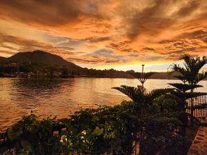 einen Sonnenuntergang über einem Wasserkörper mit Palmen in der Unterkunft PURNAMA BALIGE HOTEL in Balige