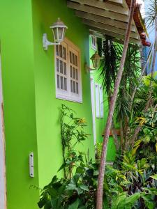 une maison verte avec une fenêtre blanche et des plantes dans l'établissement SUÍTES Caminho do Mar, à Abraão