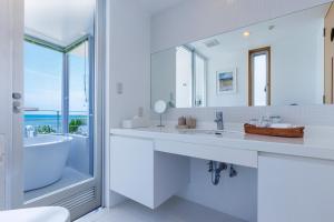 a white bathroom with a tub and a large mirror at 海まで徒歩1分 沖縄でも珍しい絶景ホテル 贅沢プライベートビーチ付き ビーチルーム in Onna