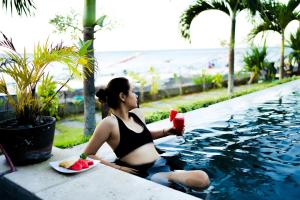 una donna seduta accanto a una piscina con un piatto di frutta di Alam Bali Beach Resort ad Amed