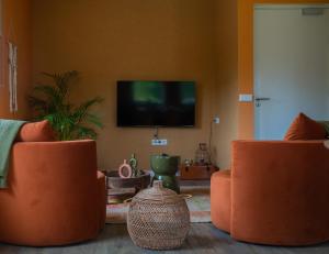 een woonkamer met 2 oranje stoelen en een flatscreen-tv bij TweeZeven in Guelle