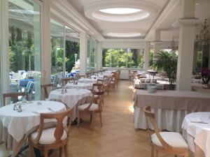 un ristorante con tavoli e sedie bianchi e finestre di Hotel Royal a Stresa