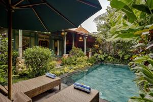 una piscina en un jardín con 2 bancos y una sombrilla en Teja Lokha Ubud Villa, en Ubud