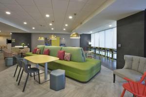 a waiting room with a green couch and tables and chairs at Home2 Suites By Hilton Holland in Holland