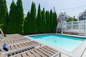 a swimming pool with chaise lounges and a fence and trees at Condo with Wading Pool Dog Welcome in Provincetown