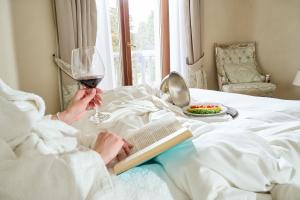 uma mulher deitada na cama com um livro e um copo de vinho em Castello Bonaria Wine & Spa Resort em Campiglia Marittima