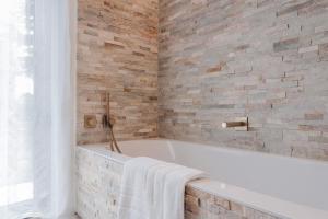 a bathroom with a white tub and a brick wall at BEE n BEE in Bruges