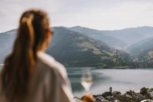 Eine Frau mit einem Glas Wein, die auf einen See schaut. in der Unterkunft Nikolaus by AvenidA Panoramic Wellness Suites in Zell am See