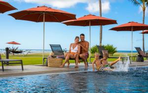 een gezin naast een zwembad met parasols bij Sheraton Kauai Coconut Beach Resort in Kapaa