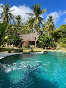 a swimming pool in front of a house with palm trees at The Papalagi Resort in Gili Gede