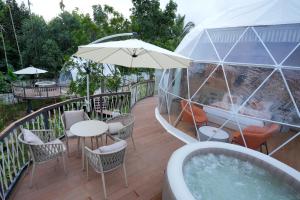 a hot tub on a deck with chairs and an umbrella at Le Villagio Resort & Domes in Sultan Bathery