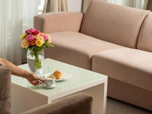 een persoon met een kopje koffie en een vaas met bloemen op een tafel bij Garni Hotel Centar in Novi Sad