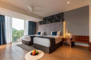 a hotel room with two beds and a table with fruit on it at De Mandarin Goa in Candolim