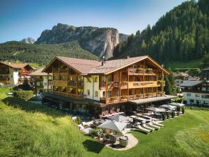 ein großes Gebäude mit Stühlen und Sonnenschirmen vor einem Berg in der Unterkunft Freina Mountain Lifestyle Hotel in Wolkenstein in Gröden