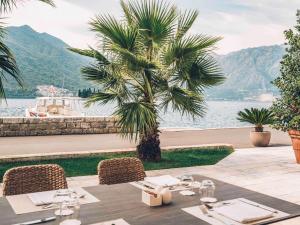 een tafel met stoelen en een palmboom naast het water bij Heritage Grand Perast By Rixos in Perast