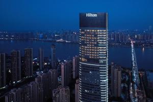 ein hohes Gebäude mit dem Hiltonschild darauf in der Nacht in der Unterkunft Hilton Changsha Riverside in Changsha