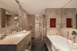 ein Badezimmer mit zwei Waschbecken, einer Badewanne und einer Dusche in der Unterkunft Hilton The Hague in Den Haag