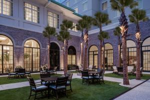 un patio con mesas, sillas y palmeras en Embassy Suites by Hilton Charleston Harbor Mt. Pleasant, en Charleston