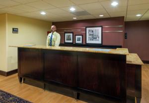 Un uomo in piedi dietro un bancone in una sala d'attesa di Hampton Inn I-10 & College Drive a Baton Rouge