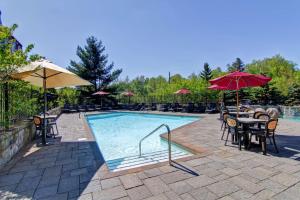 einen Pool mit Tischen, Stühlen und Sonnenschirmen in der Unterkunft Homewood Suites by Hilton Mont-Tremblant Resort in Mont-Tremblant