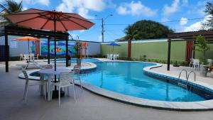 einen Pool mit einem Tisch, Stühlen und einem Sonnenschirm in der Unterkunft Hotel Enseada dos Corais in Cabo de Santo Agostinho