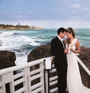 a bride and groom standing next to the ocean at The Condado Plaza Hotel in San Juan