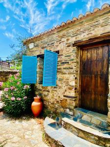 uma casa de pedra com persianas azuis e um vaso ao lado de uma porta em Casa La Rocita em Badajós