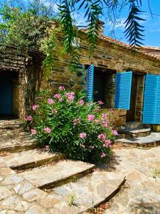 uma casa de pedra com persianas azuis e flores cor-de-rosa em Casa La Rocita em Badajós