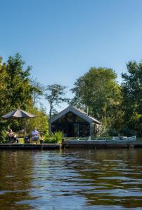 un homme assis sur un quai à côté d'une maison sur l'eau dans l'établissement Pean-buiten Waterlodges, à Nes