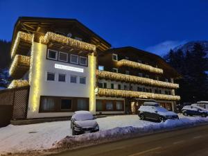 um grande edifício com carros estacionados em frente em Hotel Rododendro Val di Fassa em Campitello di Fassa