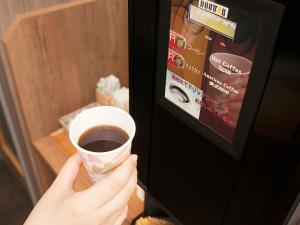 una persona sosteniendo una taza de café en una máquina expendedora en Hotel Route Inn Kato, en Kato