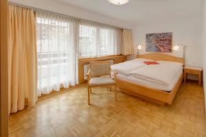 a bedroom with a bed and a chair and windows at Hotel Parnass in Zermatt