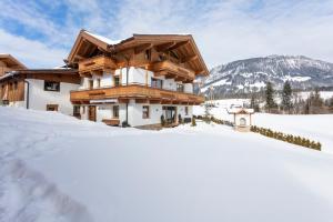 une maison dans la neige avec des montagnes en arrière-plan dans l'établissement Ferienbauernhof Stallhäusl, à Fieberbrunn