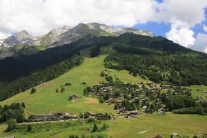 a village on a green hill with mountains in the background at Hotel Christiania in La Clusaz