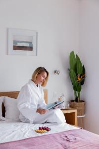 Eine Frau, die auf einem Bett sitzt und ein Buch liest. in der Unterkunft Jasmine Hotel in São Pedro de Alva