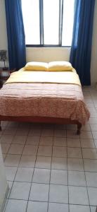 a bed in a bedroom with blue curtains and a tiled floor at Hostal Iberia in Talara