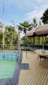 - une table et un parasol à côté de la piscine dans l'établissement Sana Riverside, à Madikeri