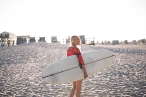 Una donna in piedi sulla spiaggia con una tavola da surf di Beach Motel St. Peter-Ording a Sankt Peter-Ording